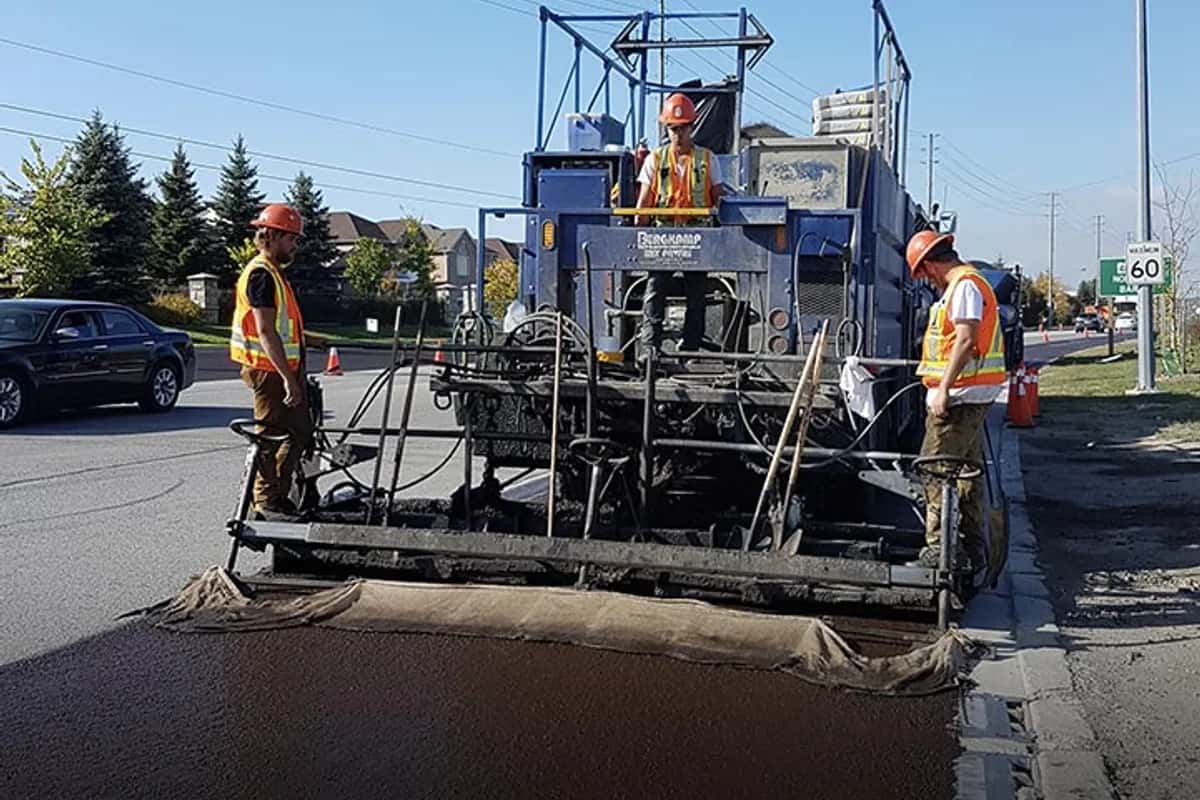 Micro-surfacing paving machine spreading polymer-modified surfacing material across a commercial street.