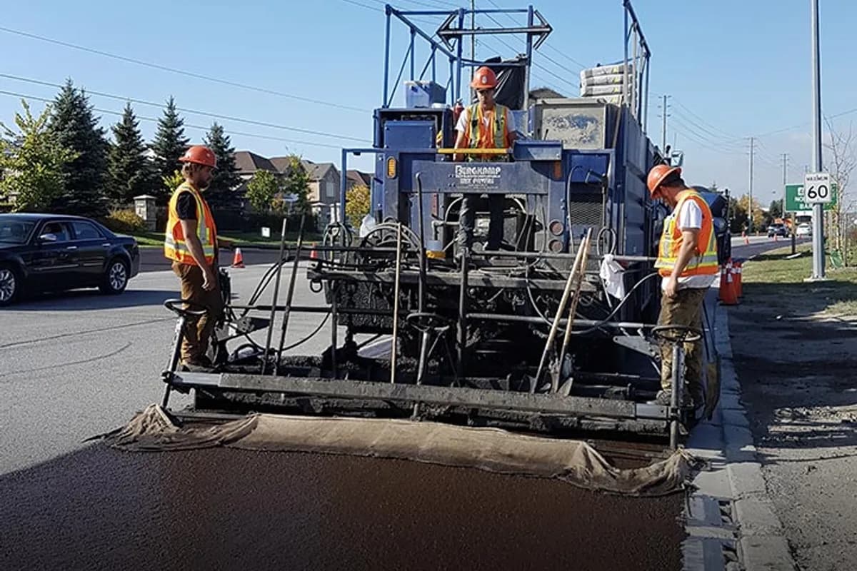 Micro-surfacing paving machine spreading polymer-modified surfacing material across a commercial street.
