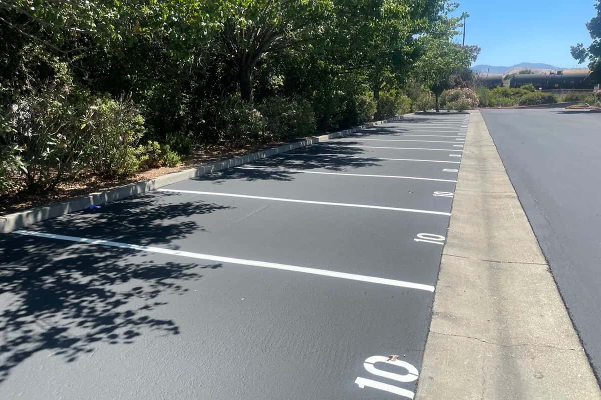 Freshly painted white parking stall lines and numbers on newly sealed dark asphalt.