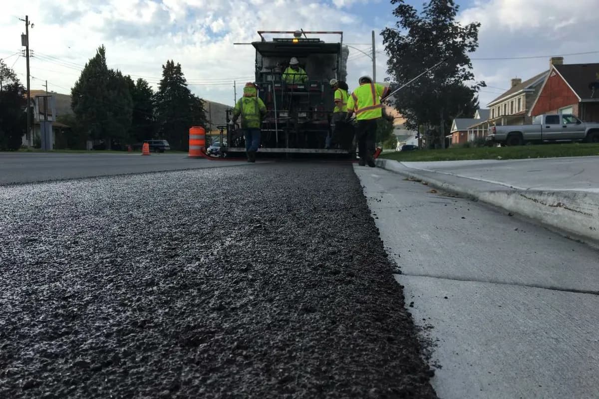Paving crew applying a fresh slurry seal mat along a residential street next to the curb.