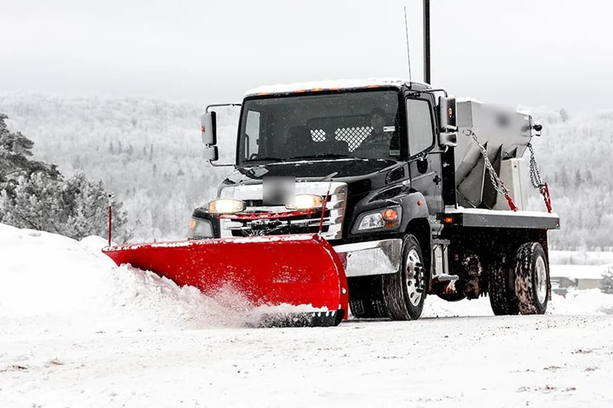Commercial snow plow truck clearing a fresh layer of snow from a lot during snowfall.