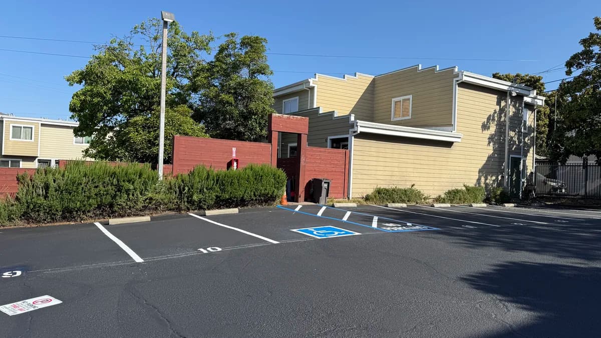 Newly painted accessible parking stall with a blue International Symbol of Accessibility, an adjoining access aisle outlined in blue and marked no parking, and fresh white stall lines on a sealcoated lot.