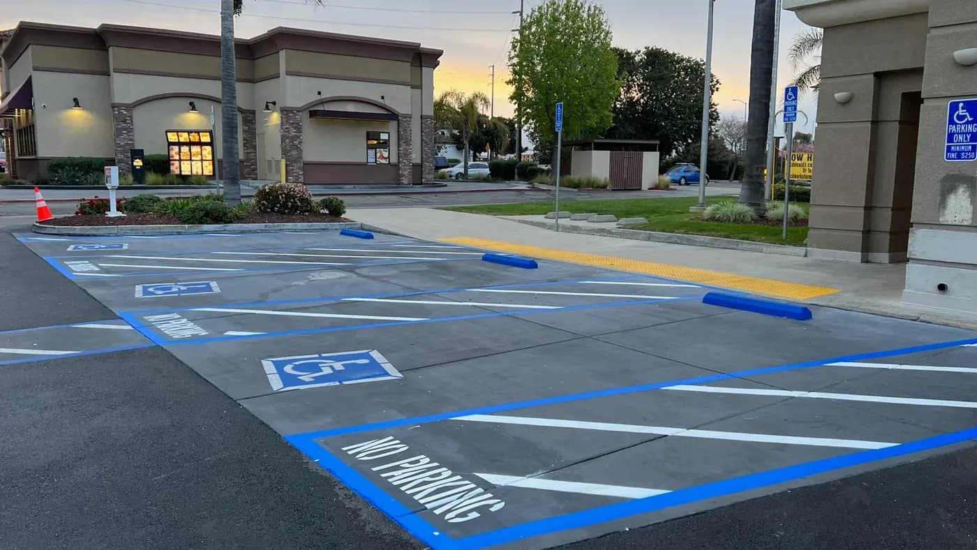 Accessible stalls with blue striping, access aisles, wheel stops, and a concrete route connecting them to the building entrance