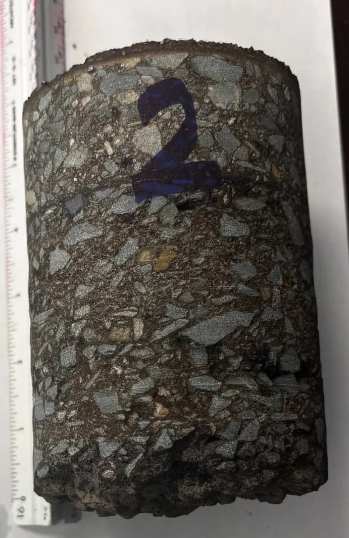 Asphalt core sample held against a tape measure to verify pavement thickness during an assessment