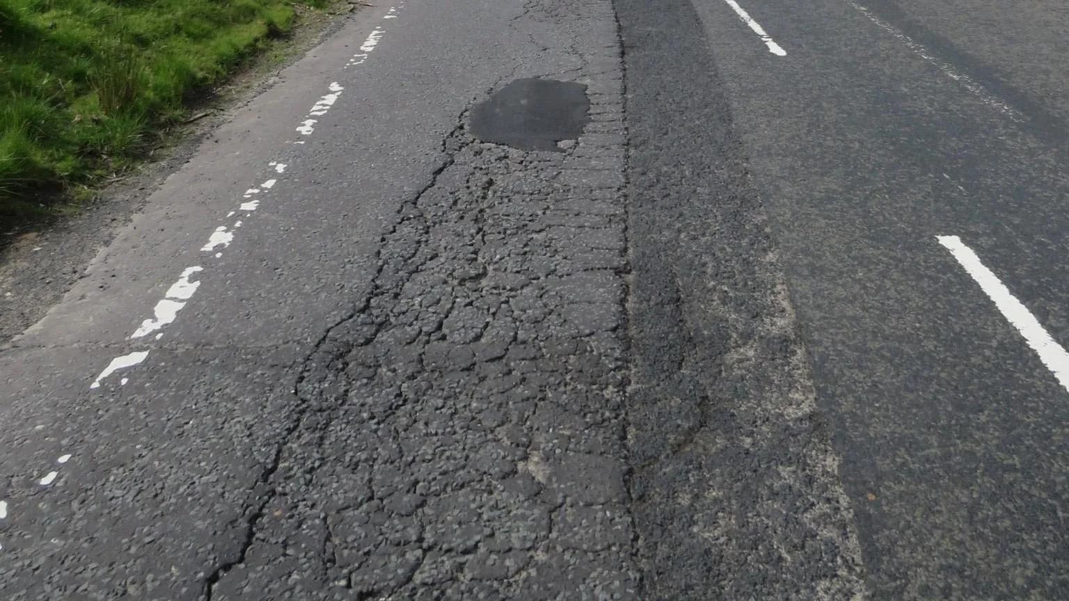 A depressed wheel path running along a lane, its surface broken into interconnected fatigue cracking with a patch at the far end, beside undamaged pavement.