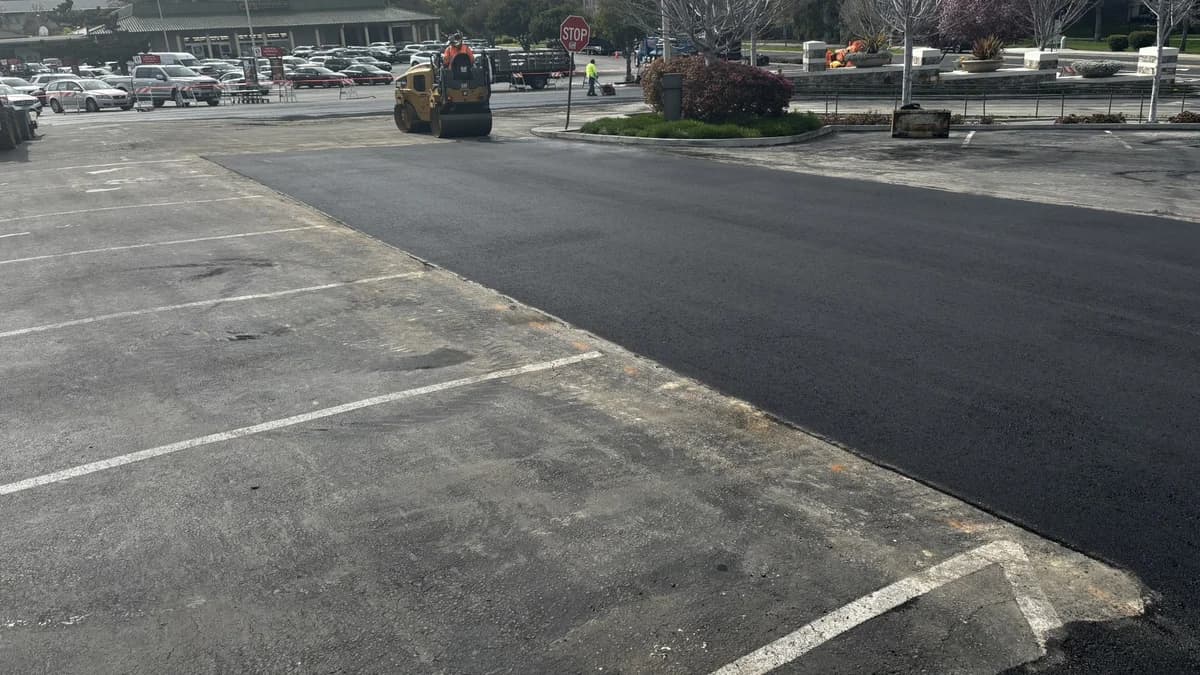 A roller compacting freshly placed asphalt in a commercial shopping center parking lot.