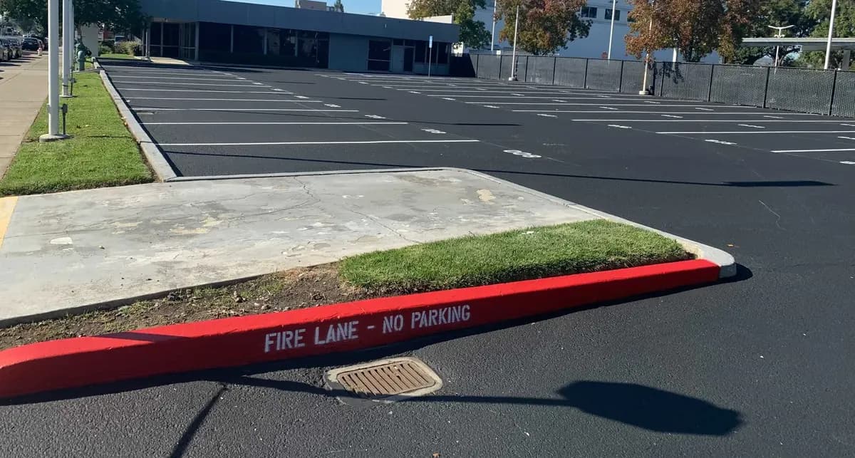 A finished commercial parking lot with a fresh black surface, new white stall striping and a red “Fire Lane – No Parking” curb