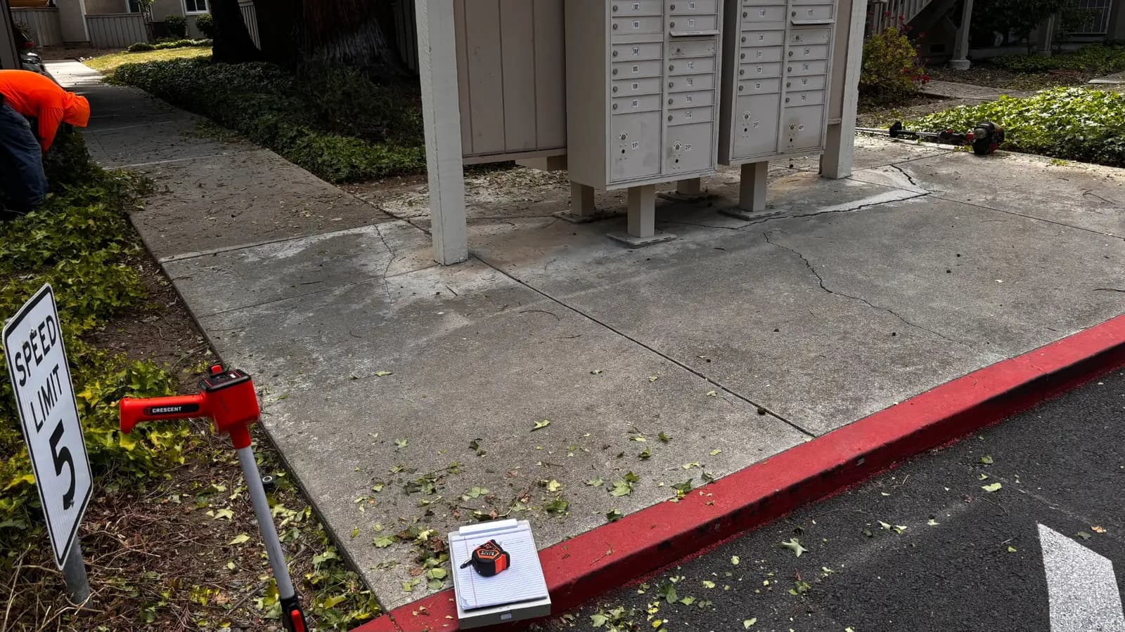 Cracked concrete pad under a mailbox cluster being measured before replacement