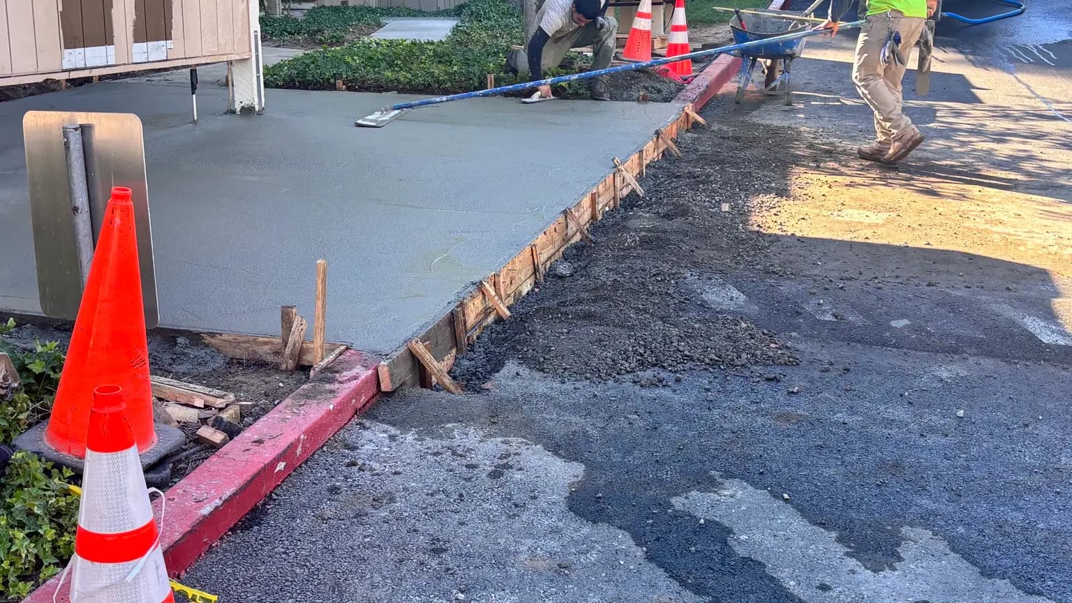 Crew screeding and finishing a freshly placed concrete pad inside timber forms