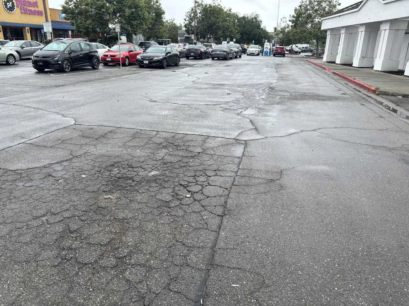 A commercial parking lot with widespread cracking and areas where the asphalt has failed through