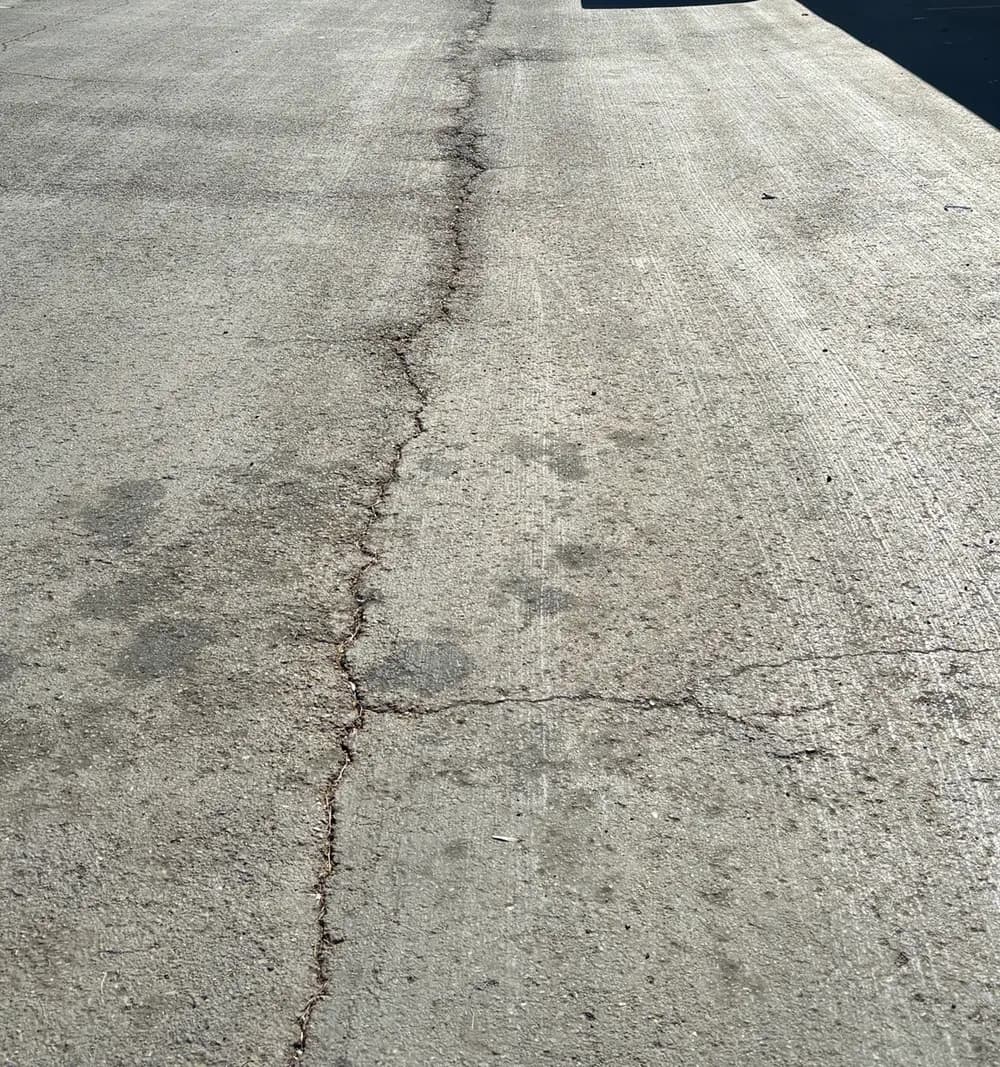 Longitudinal crack running the length of a sun-oxidized asphalt drive aisle