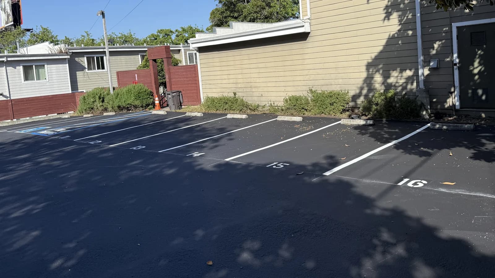 A freshly sealcoated lot striped into numbered perpendicular stalls, each with a precast wheel stop set back from the head of the space, and a blue-marked accessible stall and access aisle at the left end of the row.
