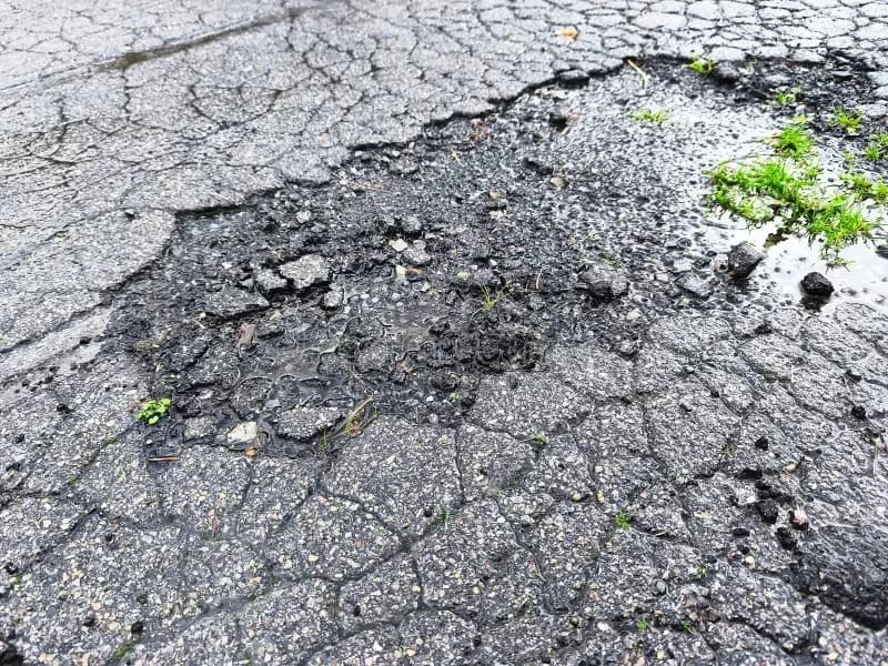 A pothole opened in a commercial parking lot where the asphalt has broken through to the base