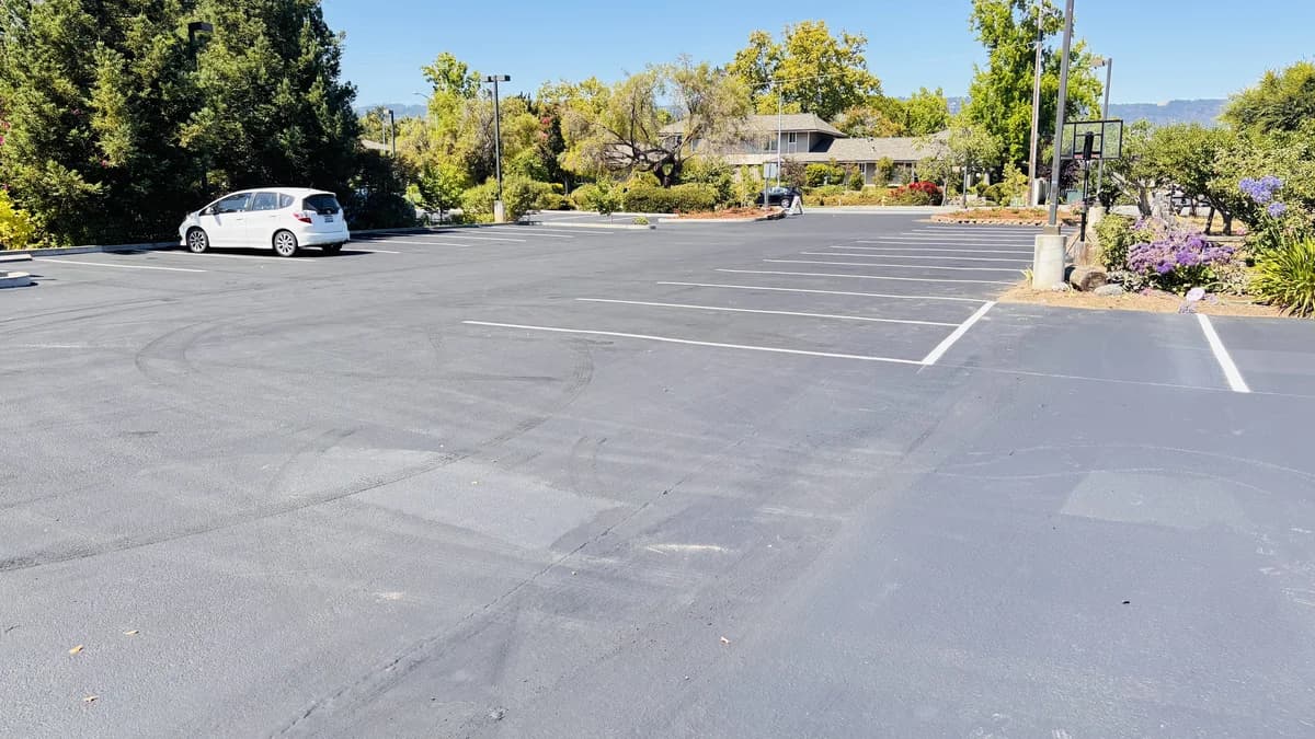 Freshly sealcoated commercial parking lot with crisp new striping and a car parked nearby.