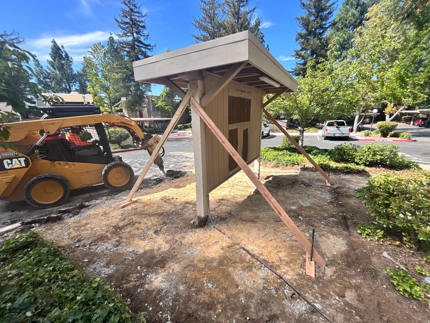 Skid steer clearing subgrade beside a mailbox shelter held up on temporary wood bracing