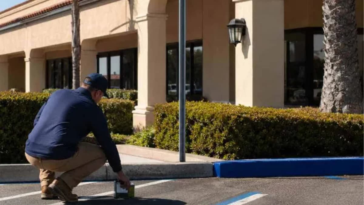 Contractor repainting blue accessible parking stall lines on sloped asphalt.